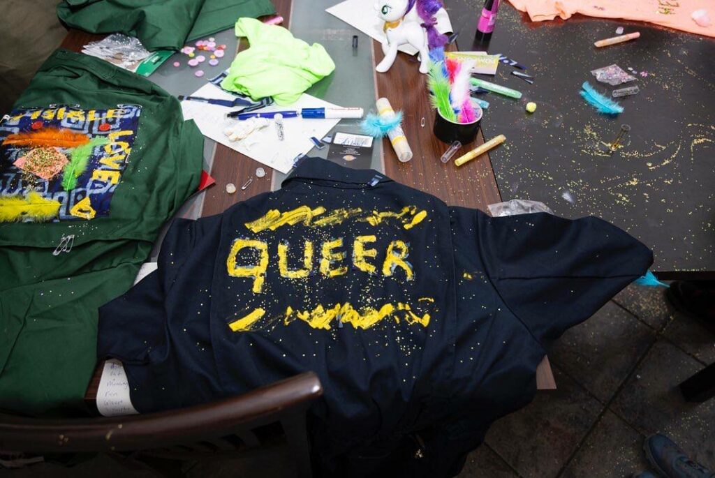 a self made decorated jumpsuit saying 'queer' in glittering letters